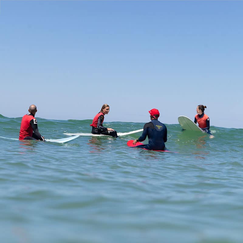 Un groupe de surfeurs assis sur leurs planches au line-up pendant un entraînement collectif à Lacanau