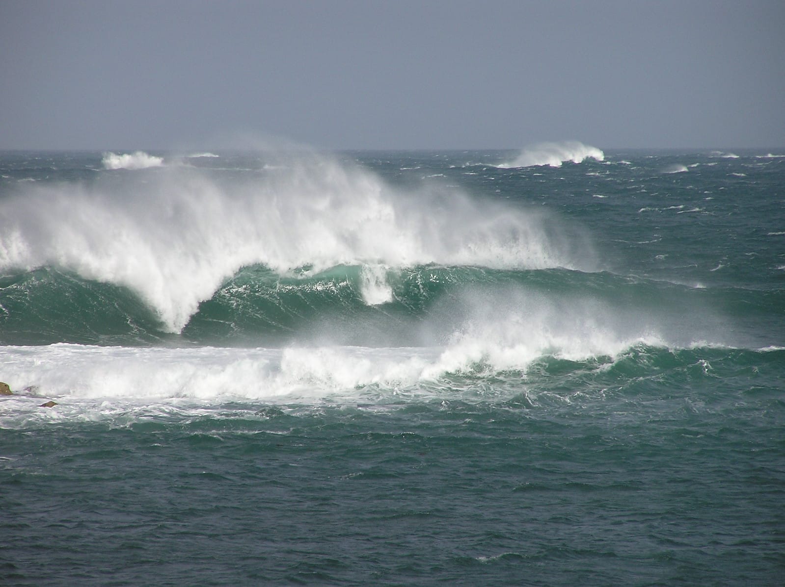 Vagues vert émeraude qui déferlent en série, crêtes arrachées par le vent, au large de la côte du Finistère