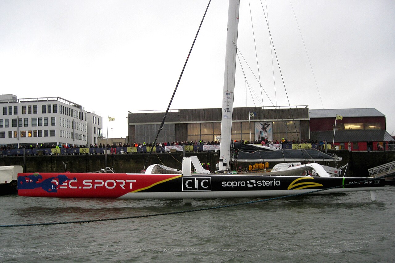 Le maxi-trimaran IDEC Sport amarré au ponton du quai Malbert à Brest, devant une foule de supportrices