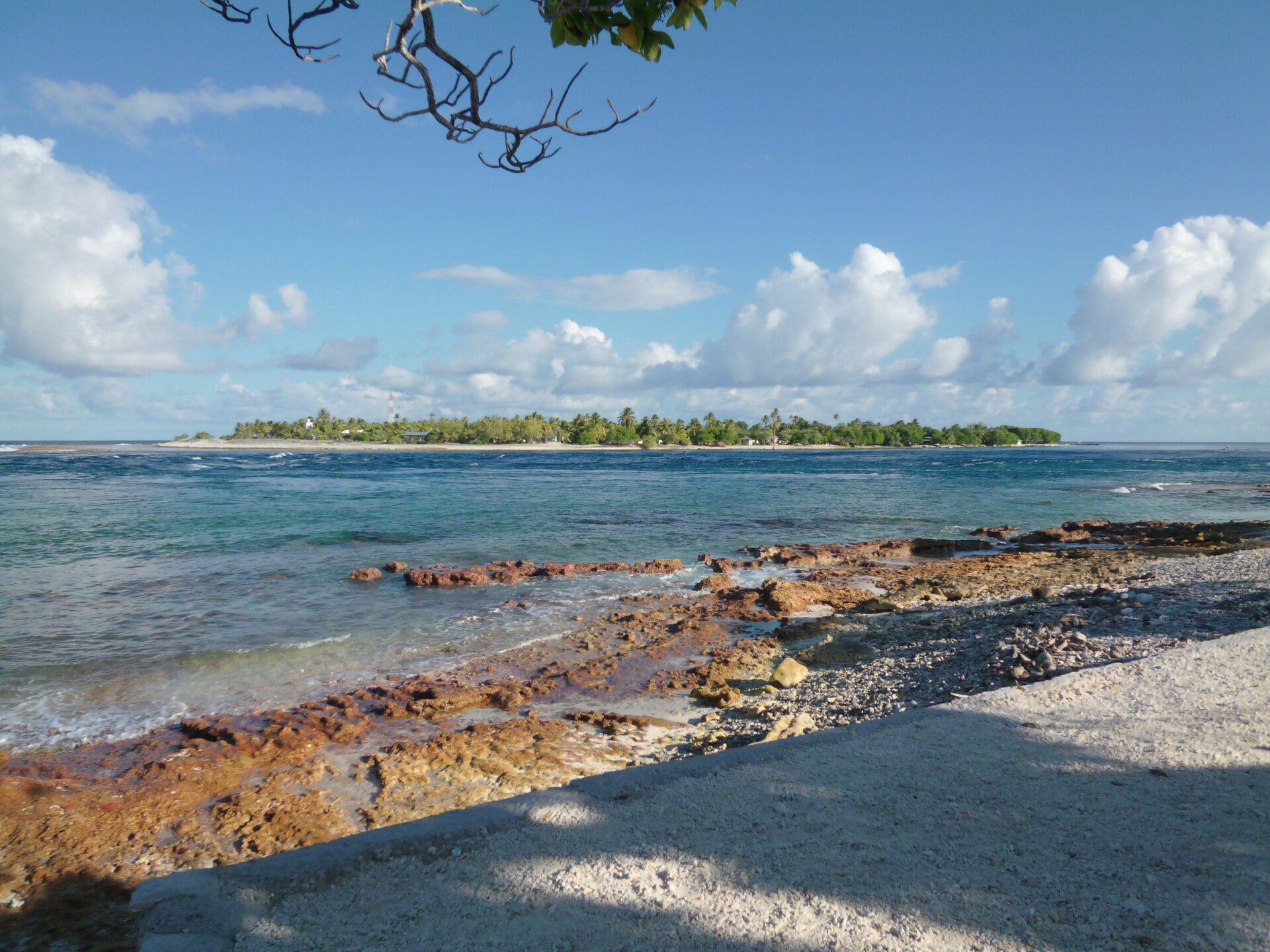 Vue de la passe de Tiputa à Rangiroa, avec le récif corallien affleurant, l'eau turquoise et un motu couvert de cocotiers à l'horizon