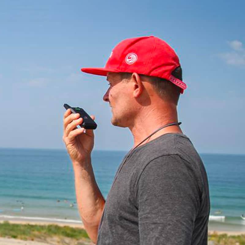 Charly Henno parle dans un émetteur radio depuis la plage pour guider un surfeur à l'eau