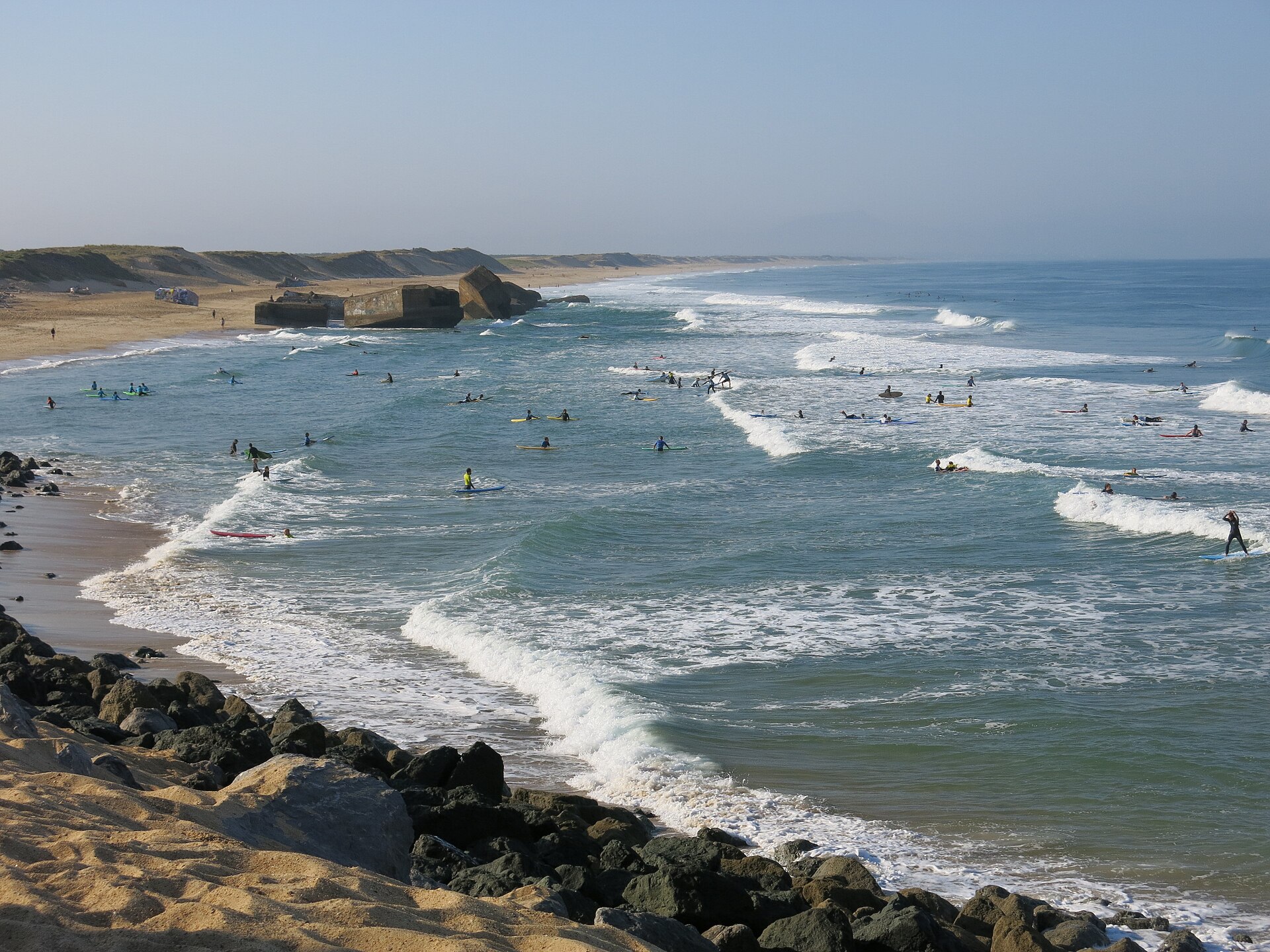 Vue de la plage du Santocha à Capbreton avec de nombreux surfeurs à l'eau et la digue en enrochement au premier plan