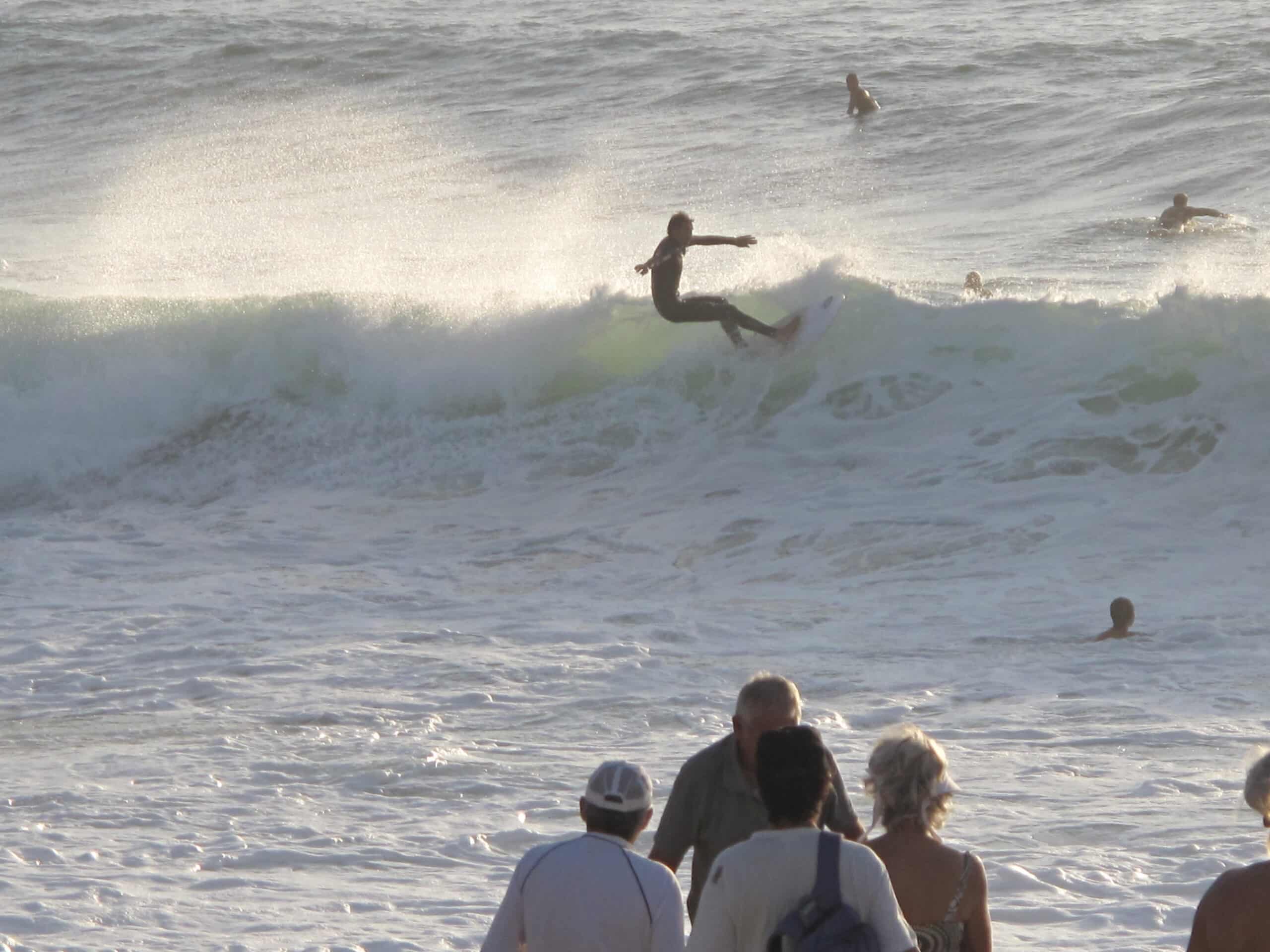Un surfeur en pleine manœuvre au-dessus de l'écume à Capbreton, observé par des spectateurs au premier plan